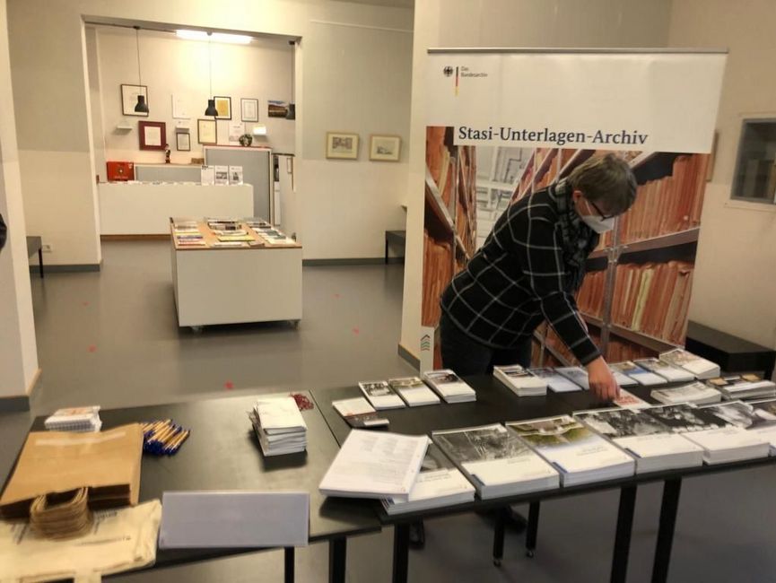 Eine Mitarbeiterin des Stasi-Unterlagen-Archivs steht hinter einem Tisch mit Informationsbroschüren. Im Hintergrund ist ein Rollup des Stasi-Unterlagen-Archivs zu sehen.