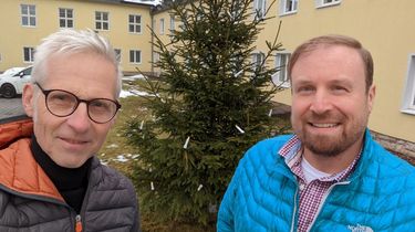 Maximilian Schönherr und Sascha Münzel stehen vor einem Weihnachtsbaum, der mit Lichtern geschmückt ist.