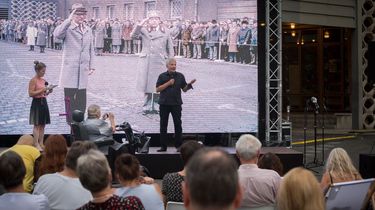 Im Hintergrund spricht Roland Jahn zu einem im Vordergrund befindlichen Publikum. Er steht vor einem großen Screen im Hintergrund, auf dem Erich Honecker und Erich Mielke vor Haus 1 zu sehen sind.