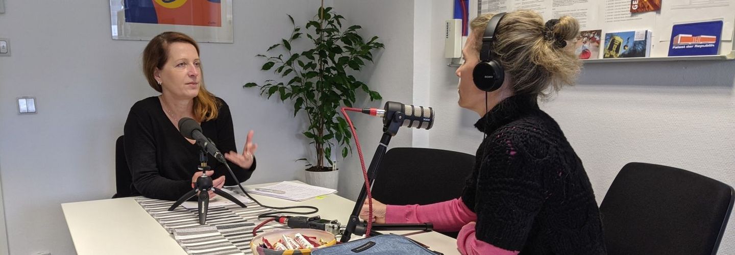 Sylvia Nagel sitzt auf der linken Seite eines Tisches und Dagmar Hovestädt rechts. Vor Ihnen stehen Mikrofone, sie sind gerade bei der Aufnahme des Podcasts.