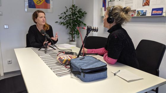 Sylvia Nagel sitzt auf der linken Seite eines Tisches und Dagmar Hovestädt rechts. Vor Ihnen stehen Mikrofone, sie sind gerade bei der Aufnahme des Podcasts.