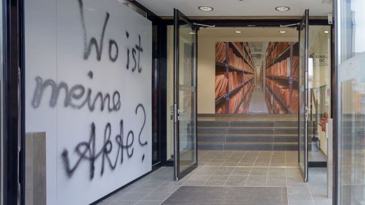 Der Eingangsbereich der Ausstellung 'Einblick ins Geheime'. Zwei Türen sind geöffnet, an der linken Seite steht an der Wand geschrieben: 'Wo ist meine Akte?'.