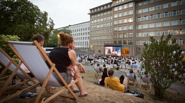 Im Innenhof der ehemaligen Stasi-Zentrale sitzen Menschen, die auf einen groen Kinobildschirm schauen.