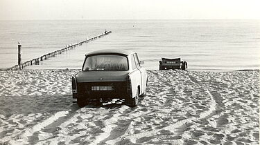 Ein Auto der Marke 'Trabant' und ein Bootsanhänger stehen auf dem Ostseestrand