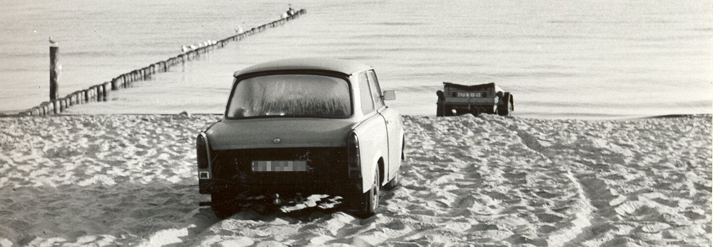 Ein Auto der Marke 'Trabant' und ein Bootsanhänger stehen auf dem Ostseestrand
