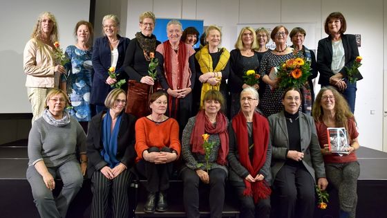 20 Frauen stehen und sitzen auf einer Bühne, viele halten Rosen in der Hand. Das Foto wurde offenbar am Ende der Buchvorstellungsveranstaltung gemacht.