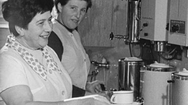 Zwei Frauen in Arbeitskitteln vor einer Kaffeemaschine.