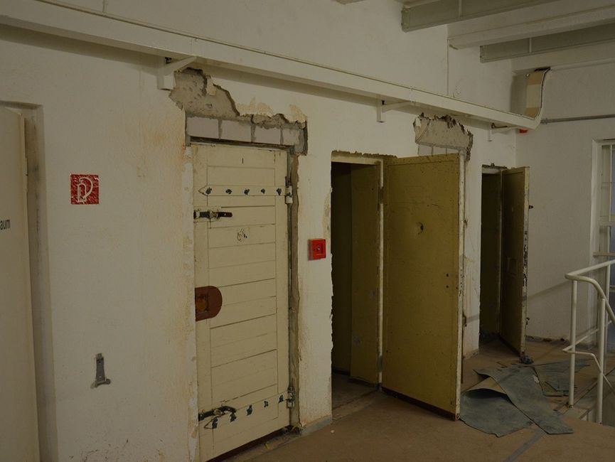 Gefängniszellen von außen. Einige Türen sind geöffnet.