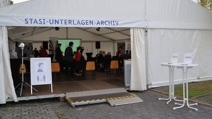Festzelt für die EinheitsEXPO 2021 in Halle mit der Aufschrift 'Stasi-Unterlagen-Archiv'. Im Innern befinden sich stehende und sitzende Besucherinnen und Besucher