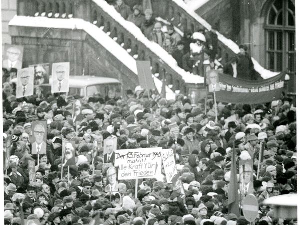 Eine große Menschenmenge demonstriert vor den Treppen eines Gebäudes. Einige der Menschen halten große Fotos von Erich Honecker und Karl Marx in die Höhe.