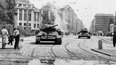Das Schwarz-Weiß-Bild zeigt eine Straßenszene am 17. Juni 1953 in Berlin. Etwas versetzt befinden sich zwei Panzer auf der Straße. Im Vordergrund sind zwei junge Männer zu sehen, die gerade Steine auf die Panzer werfen.