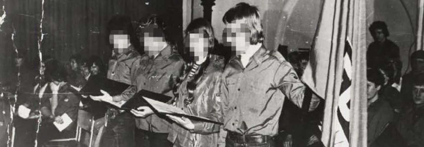 Das Bild zeigt vier Jugendliche auf einer Bühne stehend. Ganz rechts außen befindet sich eine Fahne der FDJ.
