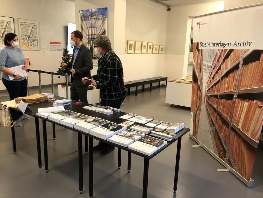 Mitarbeiter des Stasi-Unterlagen-Archivs stehen hinter einem Tisch mit Informationsbroschüren. Im Hintergrund ist ein Rollup des Stasi-Unterlagen-Archivs zu sehen.
