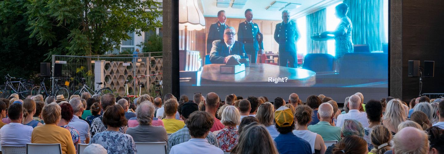 Menschen sitzen vor einer großen Leinwand und sehen den Spielfilm "Leander Haußmanns Stasikomödie".