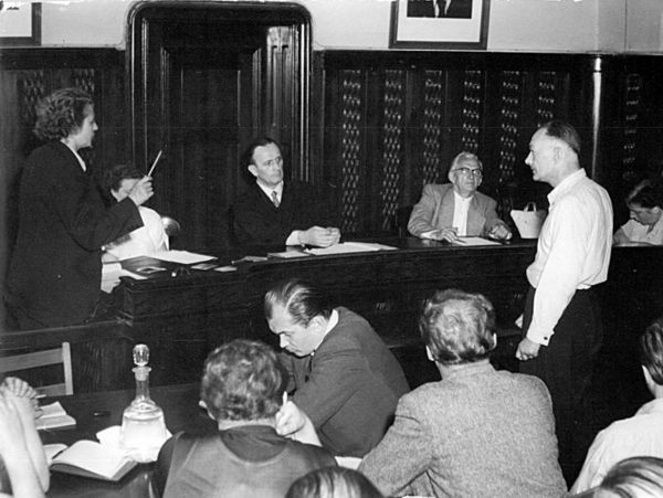 DAs Schwarz-Weiß-Bild zeigt eine Gerichtsverhandlung. Mittig im Bild steht der Angeklagte. Vor ihm sitzend der Richter.