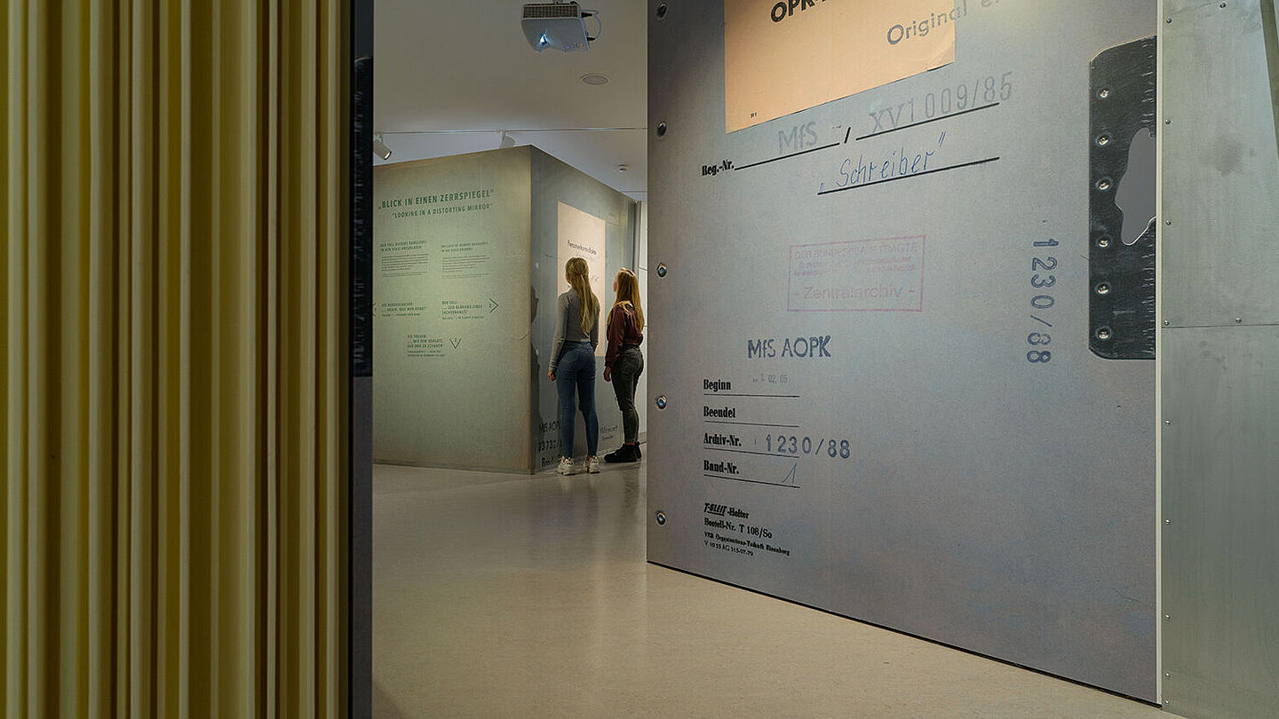 Das Bild zeigt zwei Personen in der Ausstellung Einblick ins Geheime. Sie stehen vor einem großen Aktenblatt, Quelle:
                                                <dreipc data-type="abbreviation" data-obj-uid="1" data-uid="1307">BStU</dreipc>/Dresen