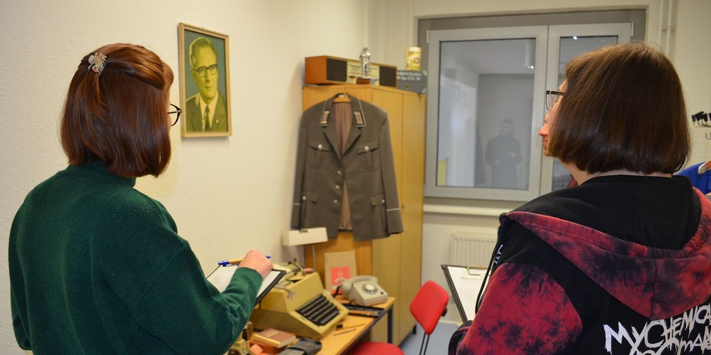 Drei junge Menschen stehen in einem Raum und sehen sich Objekte mit Stasi-Bezug an., Quelle:
            <dreipc data-type=