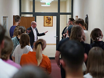 Mehrere Personen stehen in einem Gang und hören einem Mitarbeiter des Stasi-Unterlagen-Archivs zu.