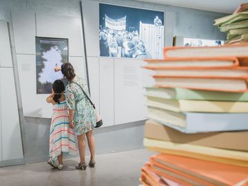 A recreated pile of files is in the centre of one of the exhibition rooms. In the background you see a woman with a child who use the touchscreen.