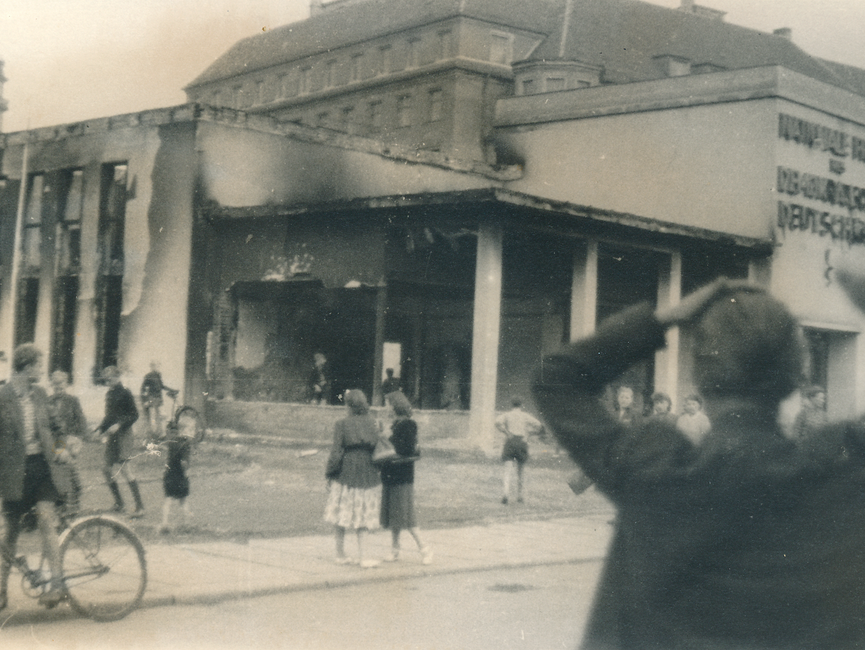 Menschen vor dem ausgebrannten Pavillon der Nationalen Front auf dem Leipziger Marktplatz. 