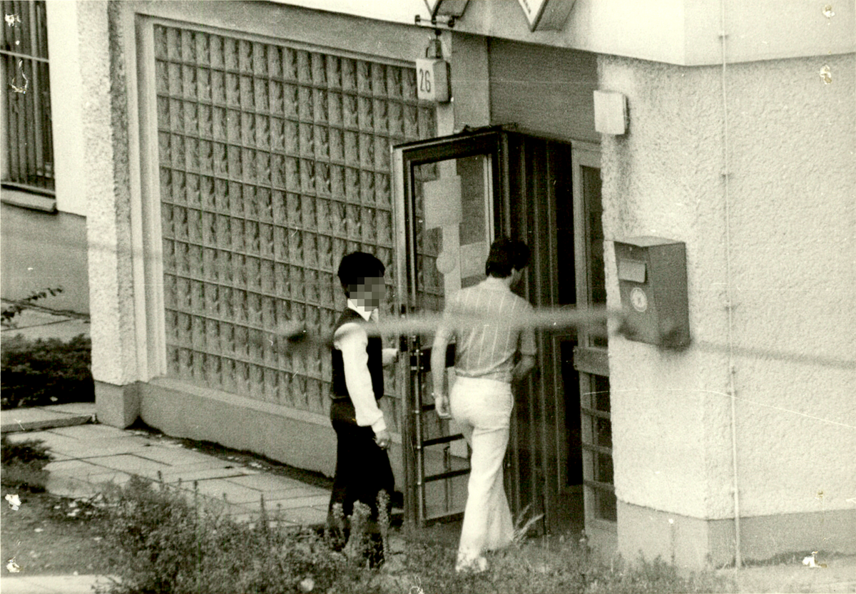 Zwei Männer betreten nacheinander ein Gebäude mit der Hausnummer 26.