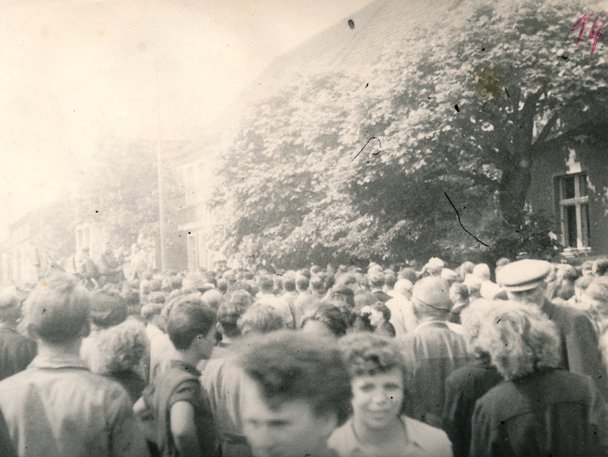Eine große Gruppe von Demonstranten auf einer öffentlichen Straße, die vor einem mit sowjetischen Soldaten besetztem Auto steht.
