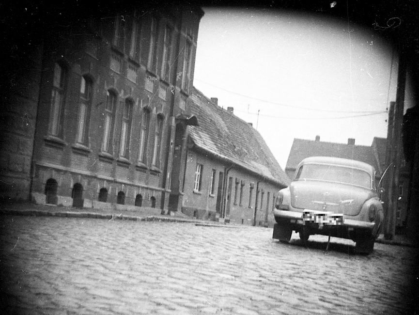 Schwarz-Weiß-Aufnahme eines Autos, vermutlich des Typs Wartburg 311, in einer unbekannten Kopfsteinpflasterstraße im DDR-Bezirk Halle. Die Häuser weisen auf eine dörfliche oder kleinstädtische Wohngegend hin.
