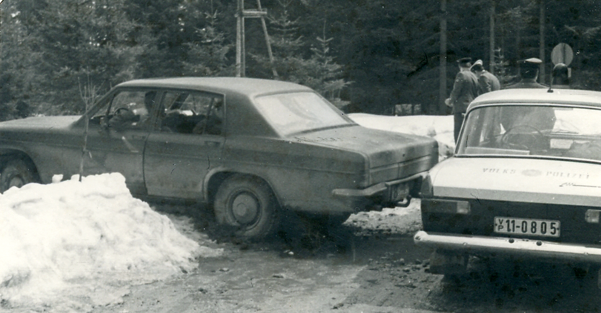 Das Bild zeigt ein Fahrzeug, das in einer Schneewehe feststeckt. Direkt dahinter befindet sich ein Fahrzeug der Volkspolizei.