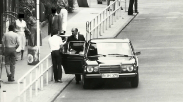 Schauspieler Robert Brown steht bei den James-Bond-Dreharbeiten am Checkpoint Charlie neben einem Auto und spricht mit einer anderen Person