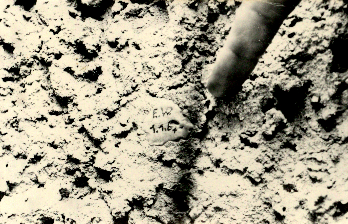 Ein Finger zeigt auf ein Stück gekneteten Brotteig in einer Mauer. Der Brotteig ist beschriftet mit "E.W. 1.1.1964".