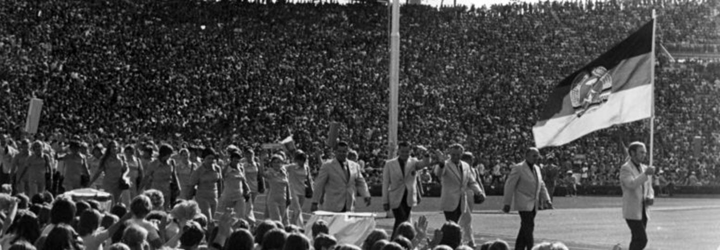Die DDR-Olympiamannschaft marschiert bei der Eröffnungszeremonie der Olympischen Spiele 1972 im Olympiastadion München ein. Ein Flaggenschwenker hält vorneweg gehend die DDR-Flagge.