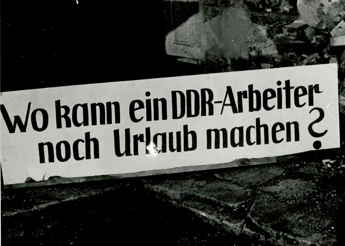 Plakat mit der Aufschrift 'Wo kann ein DDR-Arbeiter noch Urlaub machen?'.
