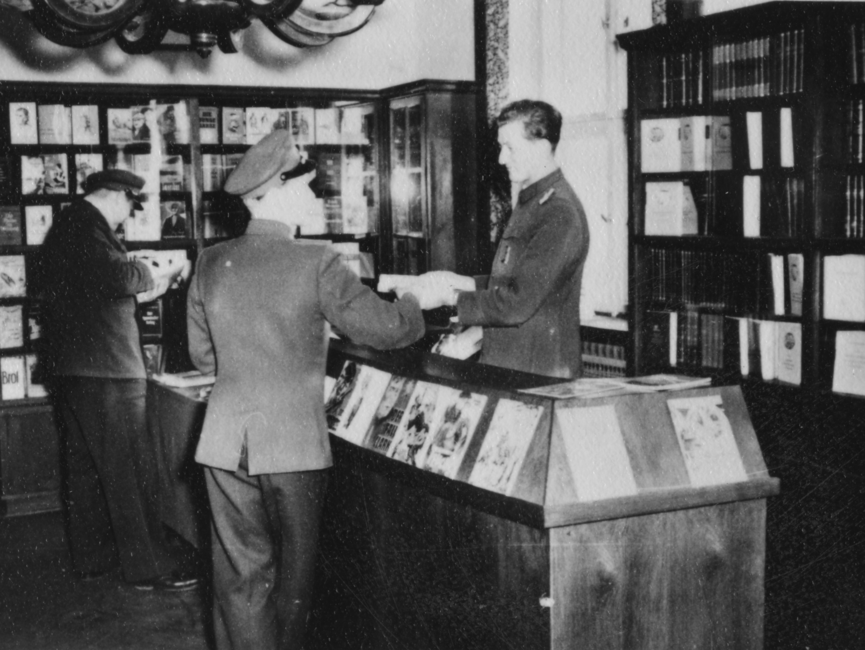 Drei JHS-Angehörige vor mehreren Bücherregalen in der Bibliothek