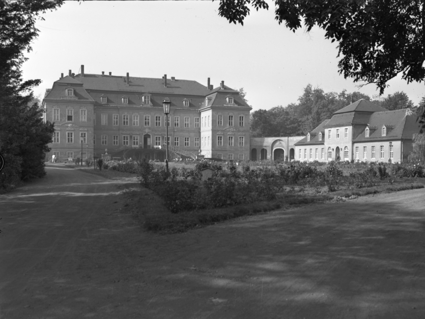 Auf dem schwarz-weißemn Lichtbild ist eine Außenaufnahme des Schloss Nischwitz, Gemeinde Thalwitz, zu sehen. AUf der rechten Seite gliedert sich ein etwas kleineres Gebäude an. Im Vordergrund ist ein mit Blumen gesäumter Rasen, umgeben von Parkwegen, zu sehen.