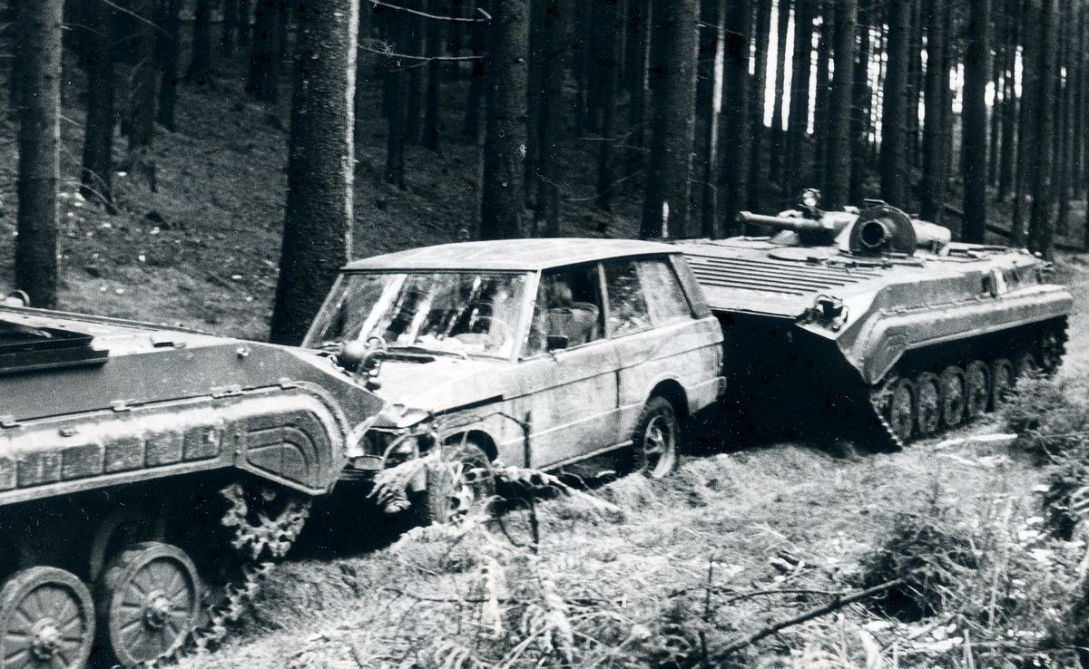 Das Bild zeigt einen von zwei Panzerwagen eingekeilten Jeep auf einem Waldweg.