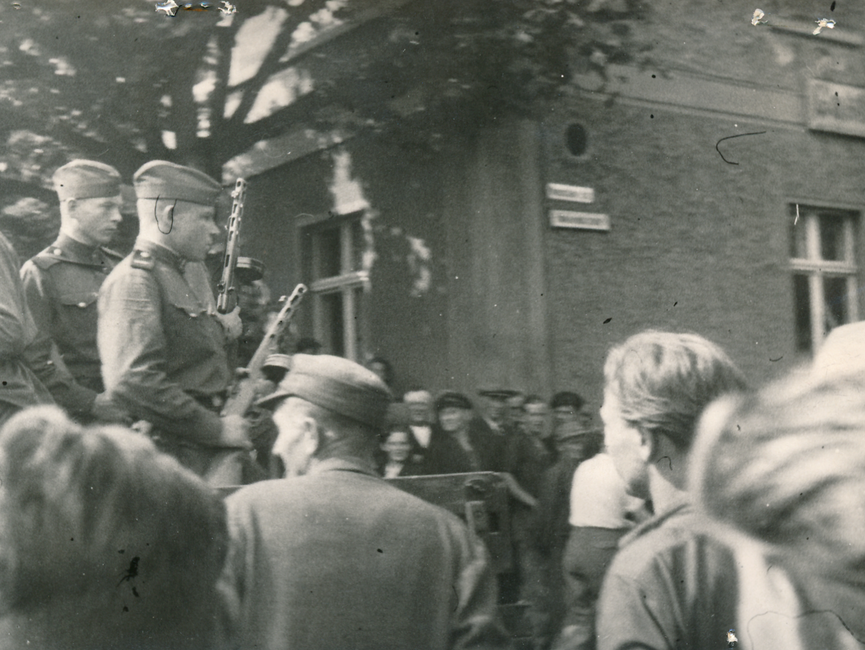 Auf dieser Aufnahme stehen sowjetischen Soldaten im Fokus. Diese sind mit einer PPSch-41 (Maschinenpistole) bewaffnetet. Um ihnen herum stehen viele Demonstranten, welche ihren Blick auf die Soldaten gerichtet haben.