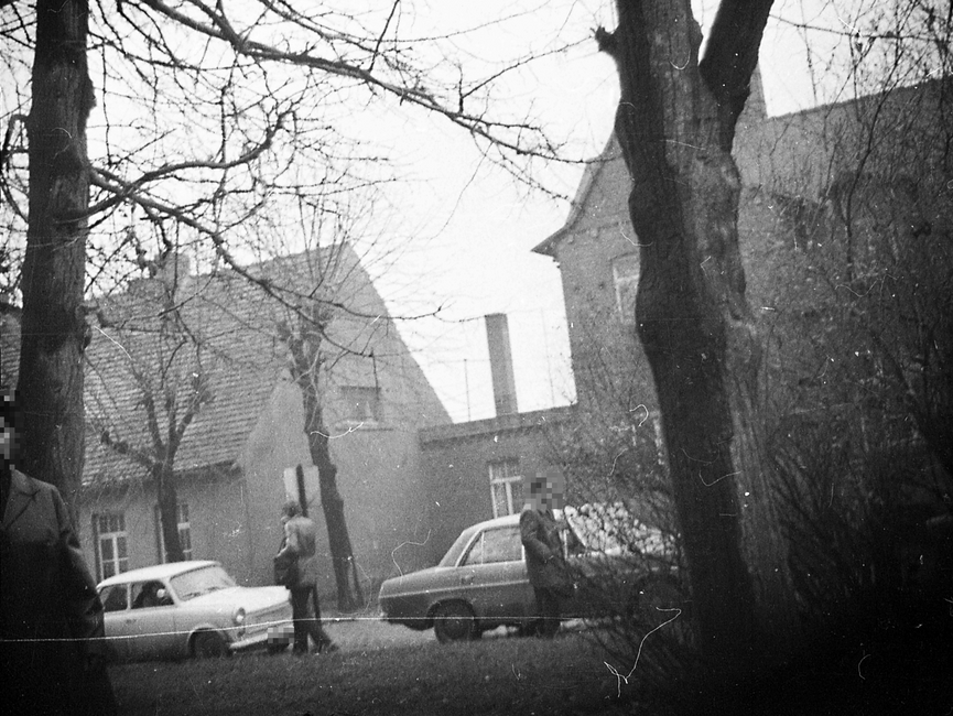 Das Foto, auf dem zwei zwischen Wohnhäusern und einem Grünstreifen geparkte Pkw, davon ein Trabant und ein Mercedes, sowie zwei männliche Personen abgebildet sind, wurde mit einer versteckten Kamera aufgenommen.